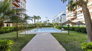 Una piscina rodeada por un jardín cuidado con palmeras y un sendero pavimentado.