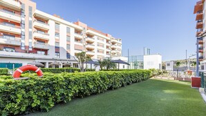 Un hotel moderno con varios balcones, un césped cuidado y mobiliario exterior con sombrillas.