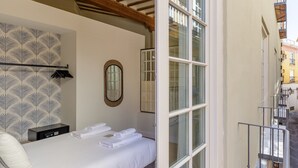 Ein Hotelzimmer mit Bett, Nachttisch, Spiegel und Fenster mit Blick auf die Straße.