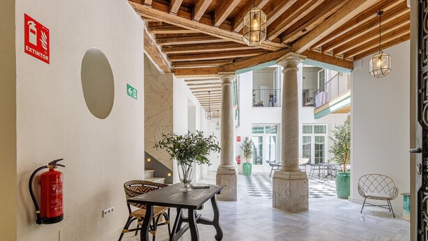 Eine geräumige Lobby mit hoher Decke, Holzbalken, einem Feuerlöscher, einem Tisch mit Stühlen und einem Blumentopf.