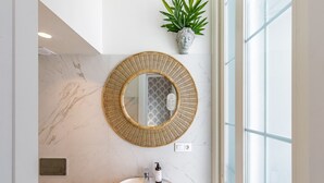 Een badkamer met een ronde spiegel, een wastafel, een plant in pot en een marmeren wand.