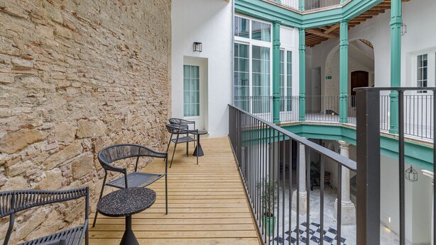 Een houten terras met buitenmeubilair, een stenen muur en een meerlaags interieur met turquoise accenten en een trap.