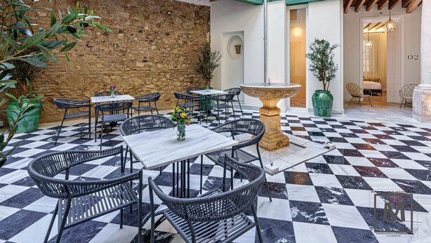 Une terrasse extérieure avec un sol à carreaux, des chaises en métal et une table centrale.
