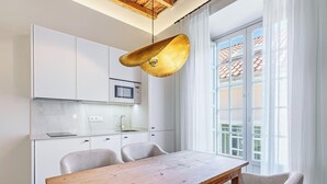 Une cuisine moderne avec des meubles blancs, une table à manger en bois et une grande fenêtre agrémentée de rideaux.