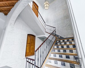 Un escalier avec une main courante en bois et des balustres noires, menant à un palier surmonté d’une porte en bois.