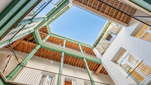 Ein mehrgeschossiges Atrium mit Holzbalken und grünen Geländern, mehreren Balkonen und einem strahlend blauen Himmel, der durch das Oberlicht sichtbar ist.