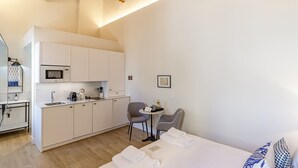 Een compacte hotelkamer met kitchenette, een klein zithoekje en een bed met keurig opgevouwen handdoeken.