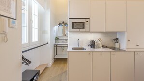 Een kleine keuken met witte kasten, een magnetron, een spoelbak en een klein aanrecht. Er is een raam dat voor natuurlijk licht zorgt en een lijst met een certificaat aan de muur.