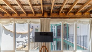 Una habitación con un ventanal grande, techo de madera y un televisor sobre un atril.