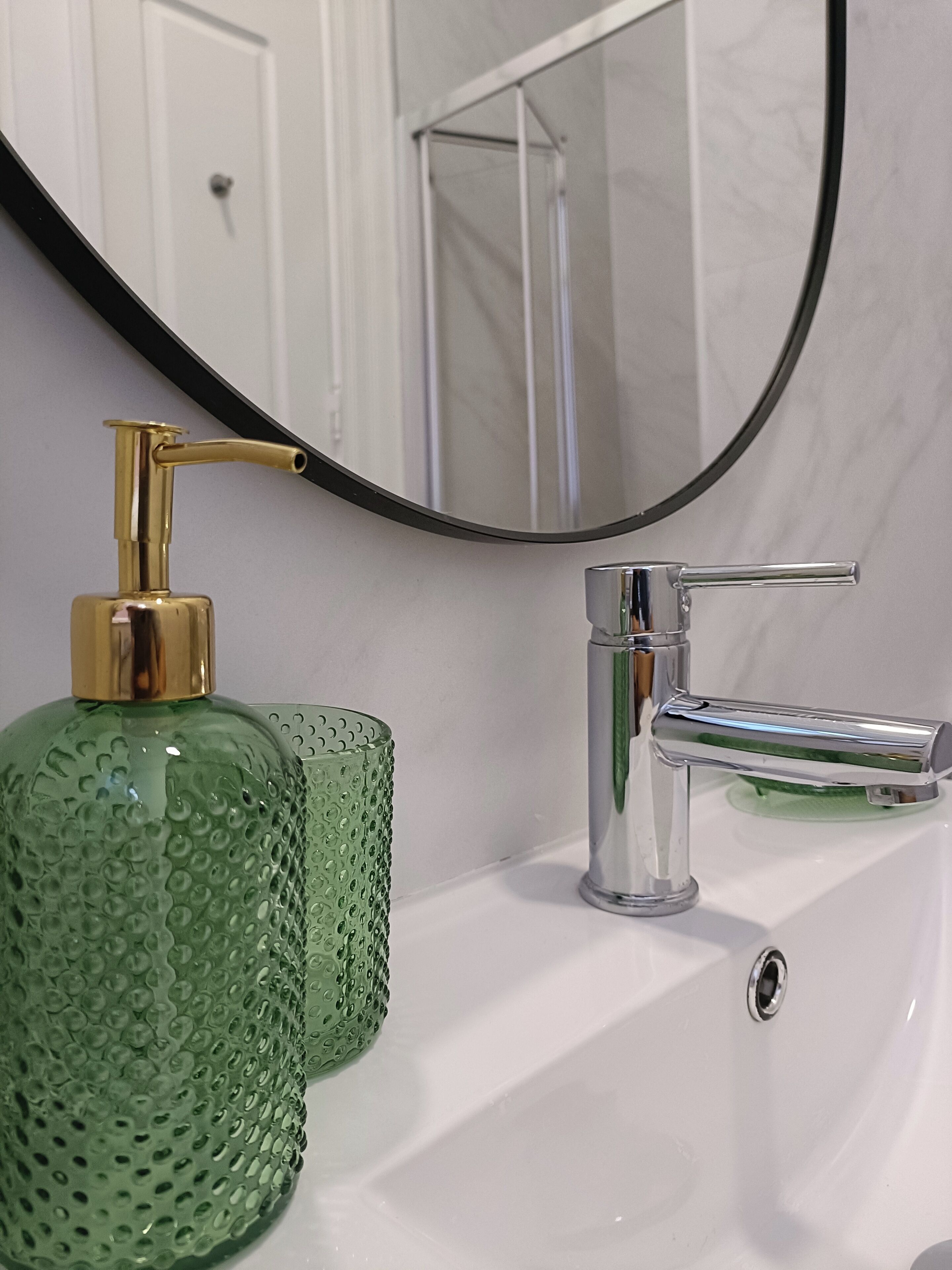 Um banheiro com uma pia branca, um dosador dourado e uma garrafa verde com textura.