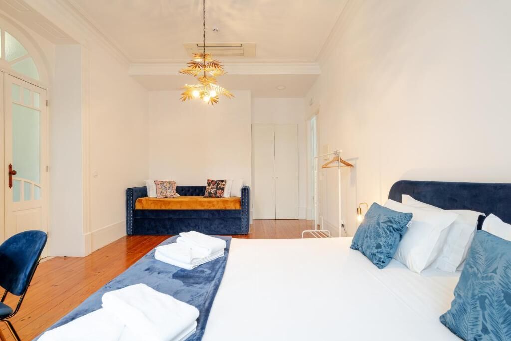A hotel room with a large bed, a sofa, a chair, and a hanging light fixture.