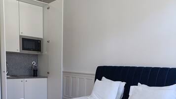 A hotel room with a bed, a bedside table with towels, a microwave, a small kitchen area, and a dark blue headboard.