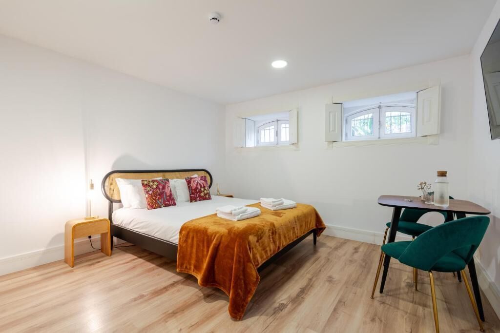 A hotel room with a bed, a small table, a chair, and two windows.