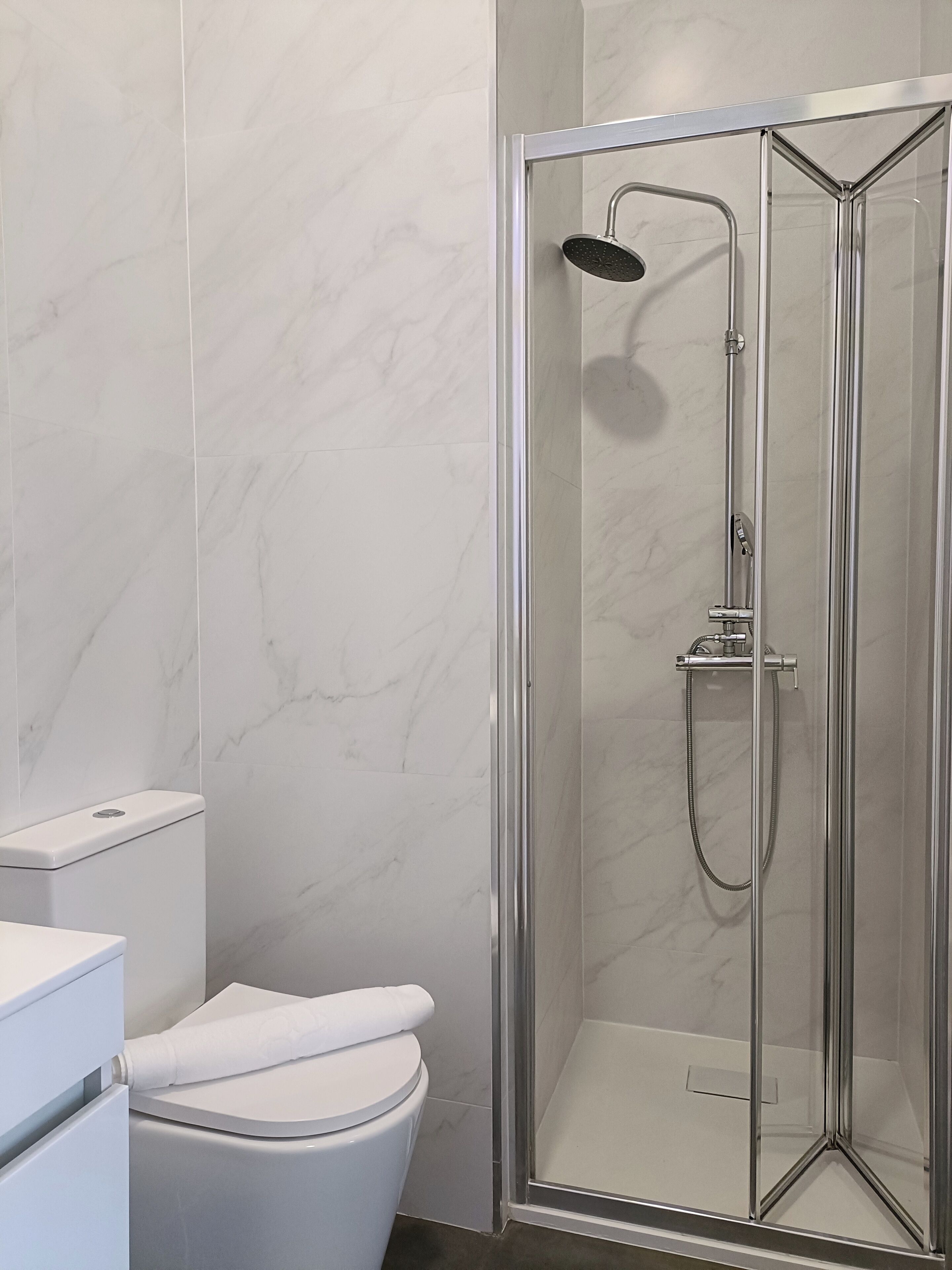 A bathroom with a glass-enclosed shower, a toilet, and a sink.