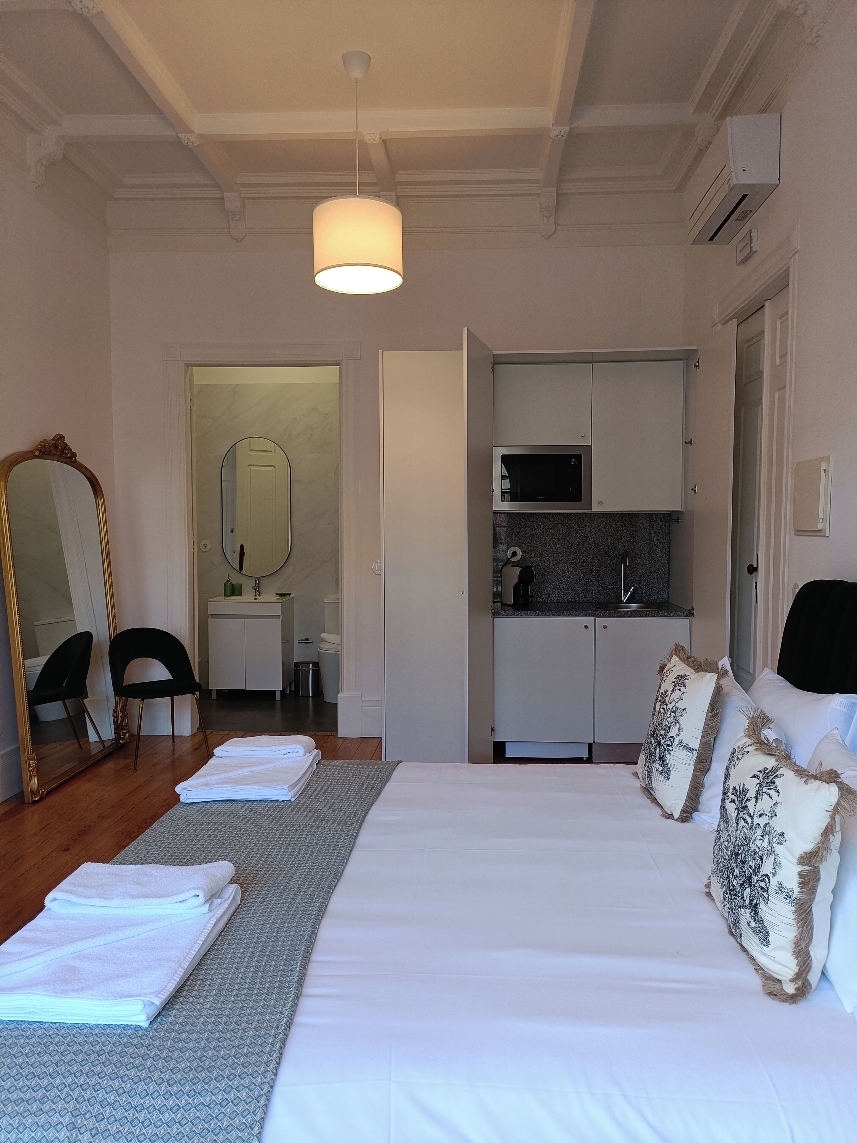 Een hotelkamer met een groot bed, een zithoek met een spiegel en stoelen, een kitchenette en een badkamer die door een open deur zichtbaar is.