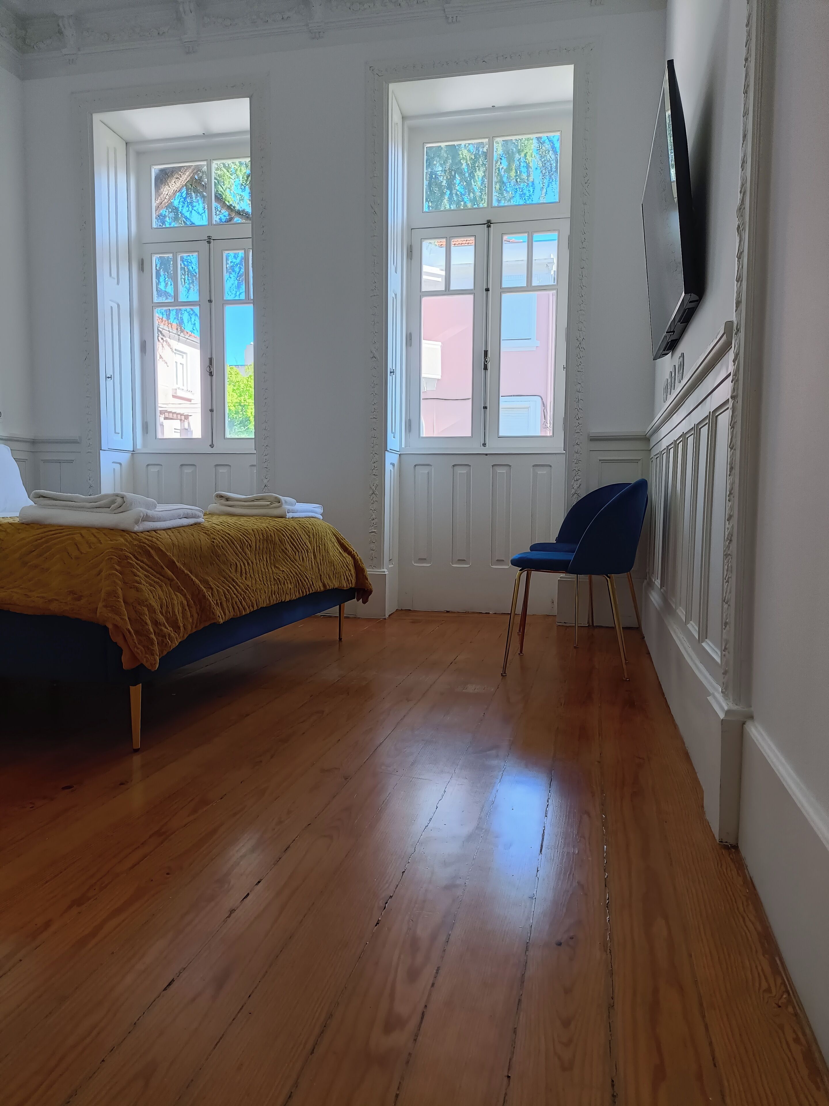 A bedroom with a bed, two windows, a chair, and a TV mounted on the wall.
