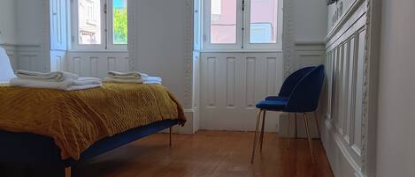 A bedroom with a bed, two windows, a chair, and a TV mounted on the wall.