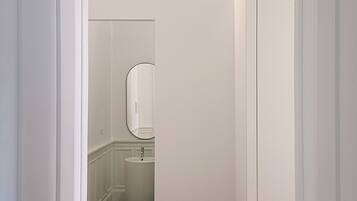 A narrow hallway with a wooden floor leading to a bathroom with a white sink and a mirror.