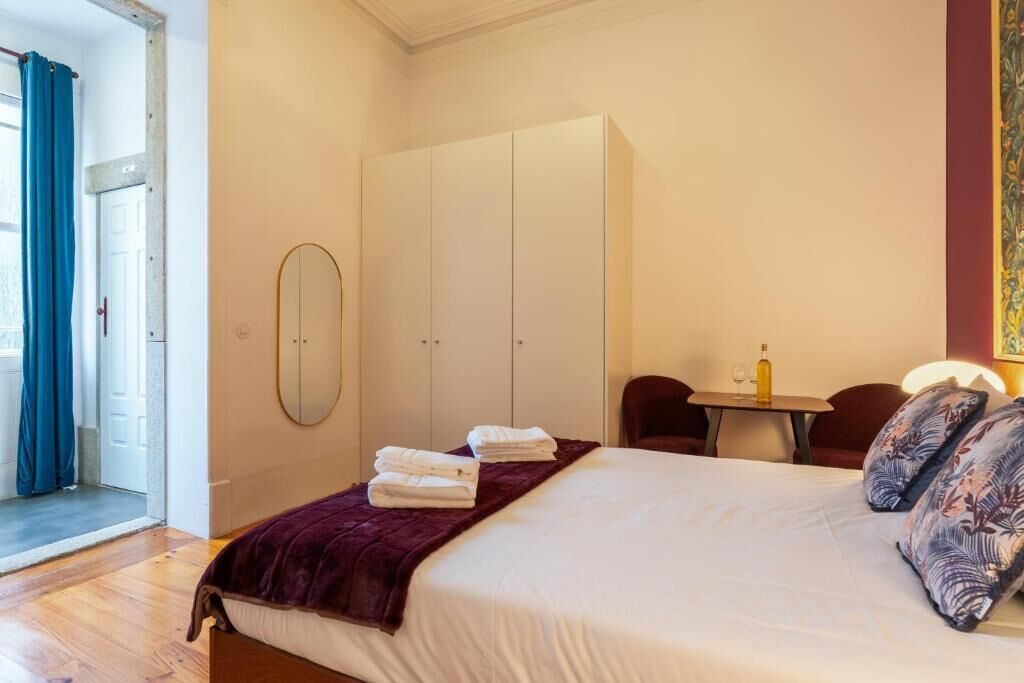 Een slaapkamer met een bed, een kledingkast, een spiegel, een tafel met een fles en een stoel.