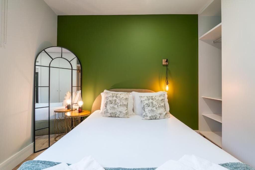 Een slaapkamer met een bed, nachtkastje, spiegel en een groene wand.