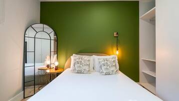 Een slaapkamer met een bed, nachtkastje, spiegel en een groene wand.