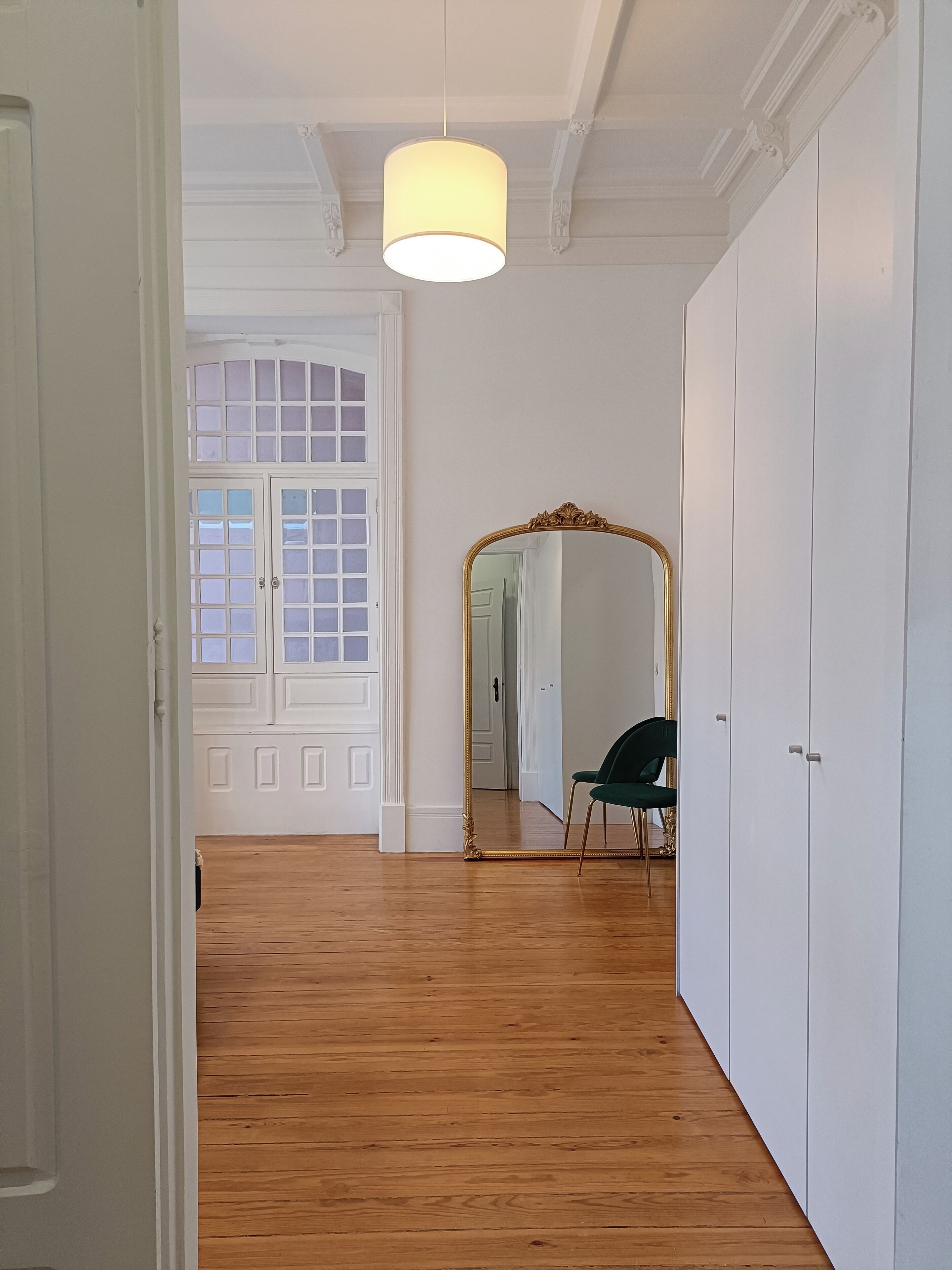A hallway with wooden flooring, white walls, a large mirror, and a hanging light fixture.