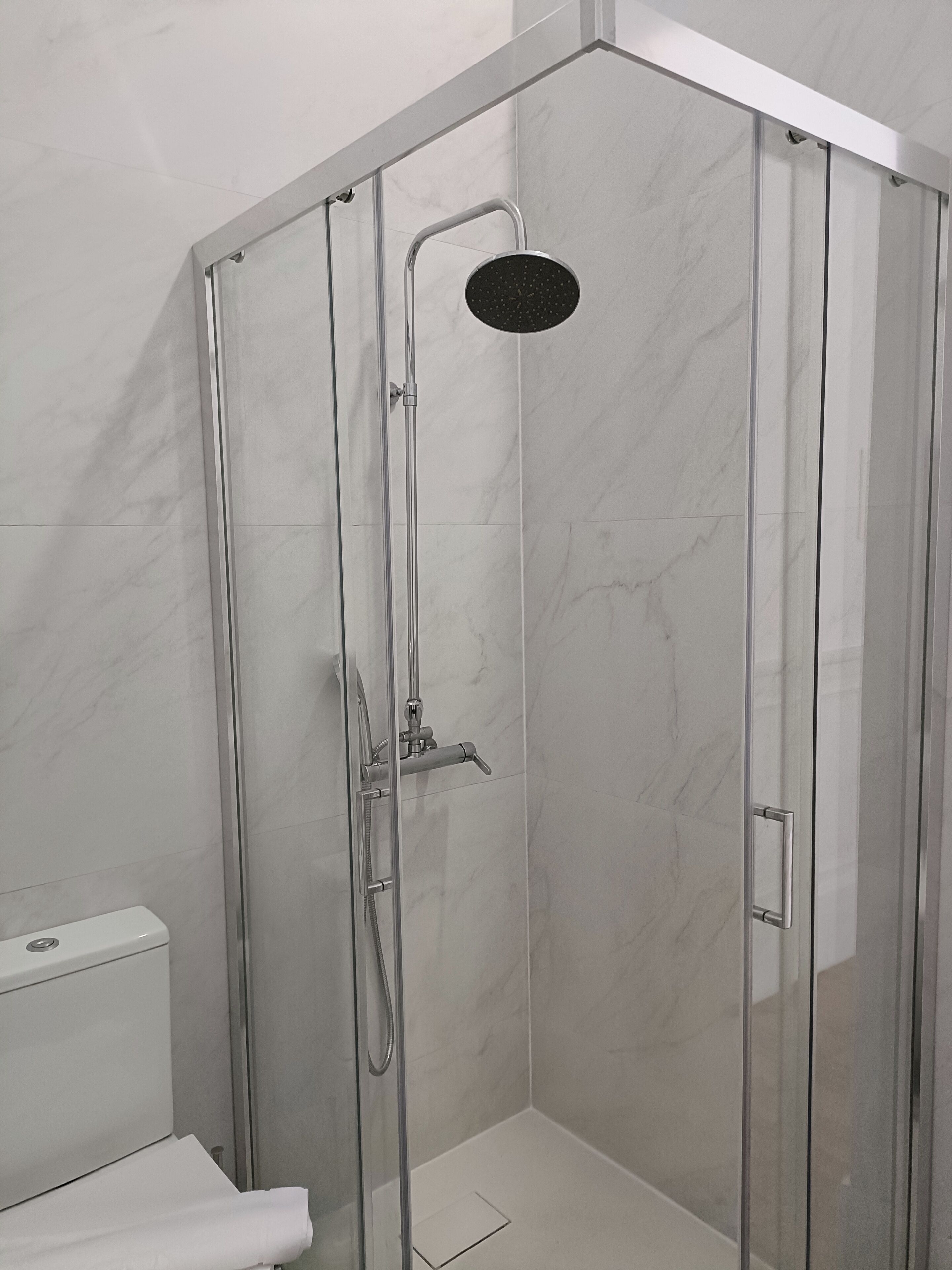A glass-enclosed shower stall with a handheld showerhead and a wall-mounted control panel.