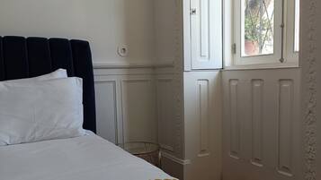 A neatly made bed with white linens, a dark headboard, and a window with a view of greenery outside.