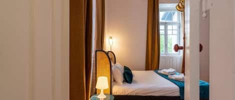 Une chambre à coucher avec un lit, une table de chevet avec une lampe et une fenêtre avec des rideaux.