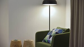 A room with a green armchair, a black floor lamp, and two wooden stools.