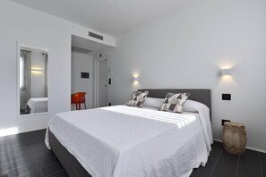 A modern bedroom with a large bed, two wall-mounted lights, a mirror, and a red chair. - Villa Fronte Mare Stornello 2 - ... (Favignana)