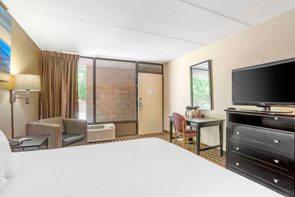Habitación de hotel con una cama, un escritorio, una silla, un televisor y una puerta corrediza de vidrio.