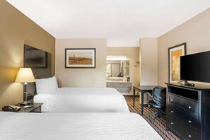 Ett hotellrum med två sängar, ett skrivbord, en stol, en byrå, en lampa, en tv och en tavla på väggen.