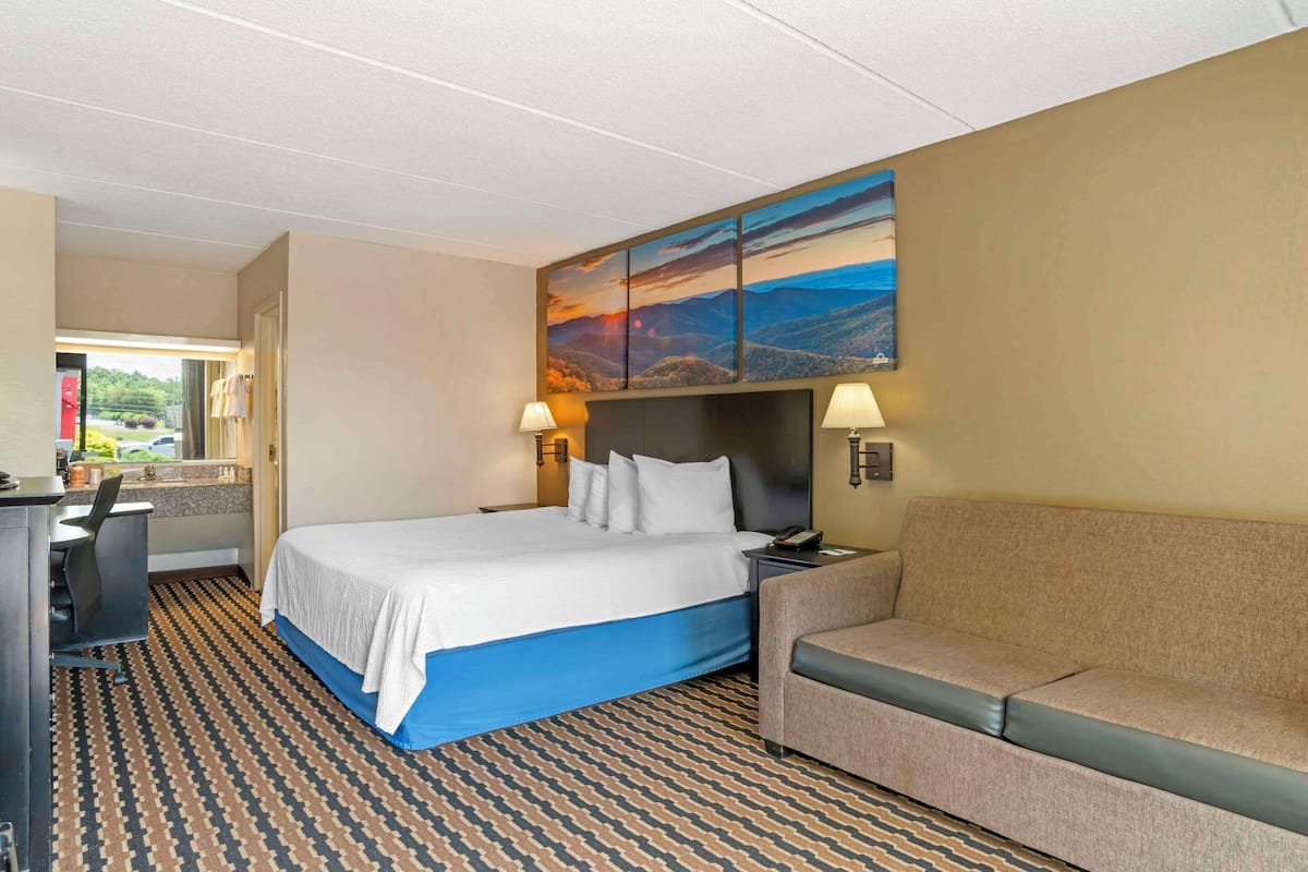 Una habitación de hotel con una cama grande, un sofá, un escritorio y un cuadro en la pared.