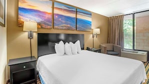 Une chambre d’hôtel avec un grand lit, une tête de lit, une table de chevet, un bureau, une chaise et une fenêtre avec des rideaux.