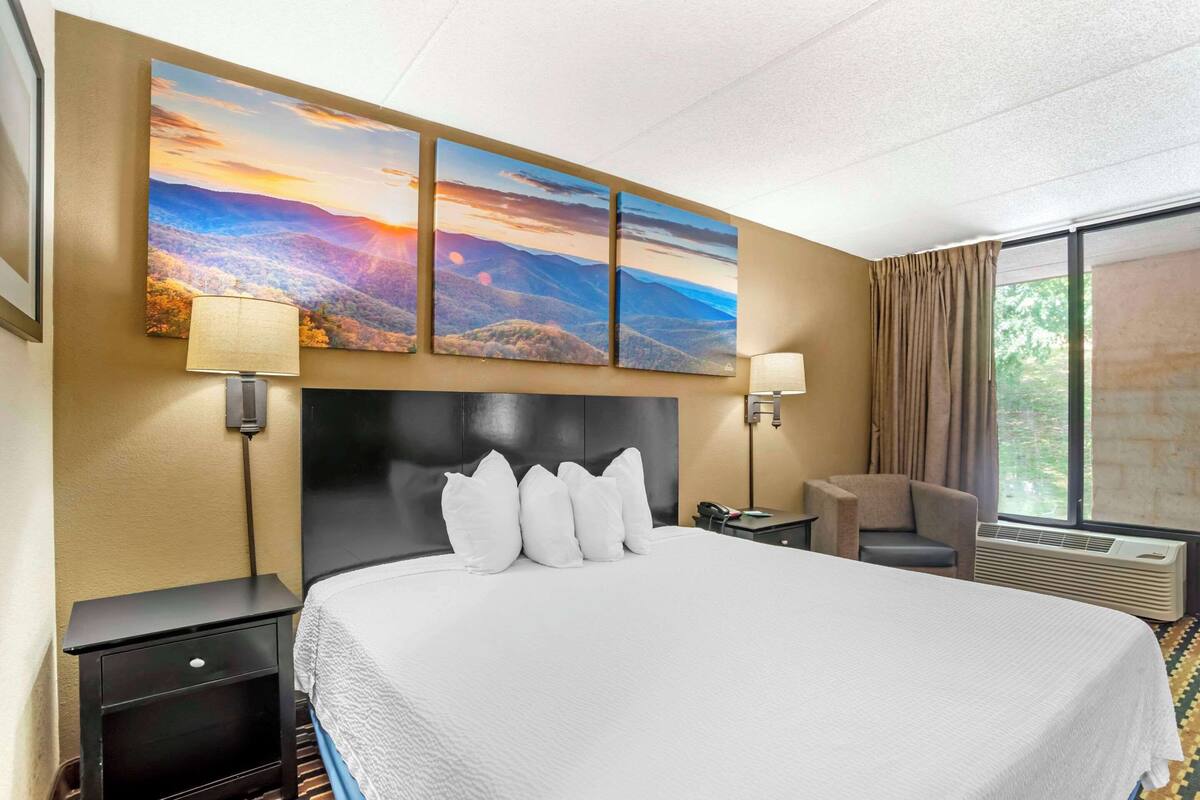 Habitación de hotel con una cama grande, cabecera, mesita de noche, escritorio, silla y ventana con cortinas.