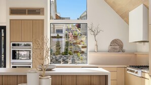 Et moderne køkken med indbyggede apparater, et stort vindue med udsigt over en have og et minimalistisk design.