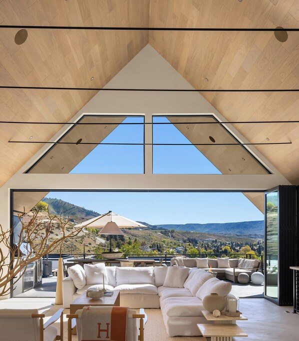 A spacious living area with a high ceiling, a large sectional sofa, and a view of a hilly landscape. - Scandinavi Inn  (Chelan)