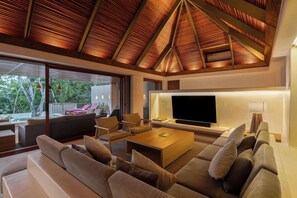 A modern living room with a large flat-screen TV, comfortable seating, and a view of the outdoors.