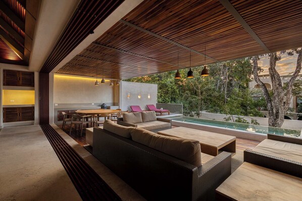 A modern outdoor living area with a pool, wooden ceiling, and seating arrangements.