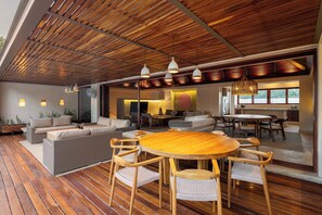 A spacious living area with a wooden ceiling, a round wooden table with chairs, and a sofa.