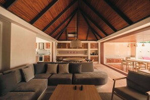 A modern living room with a wooden ceiling, a sofa set, a coffee table, and a kitchen area visible through an open door.