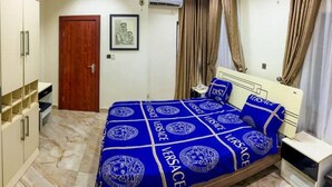 A bedroom with a bed covered in blue and white bedding, a wardrobe, a door, and a framed picture on the wall. - Home Away From Your Home (Lagos)