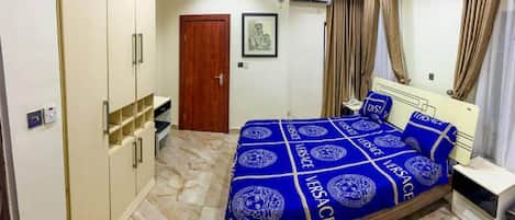A bedroom with a bed covered in blue and white bedding, a wardrobe, a door, and a framed picture on the wall.