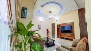A modern living room with a large TV, comfortable seating, and a ceiling with recessed lighting. - Home Away From Your Home (Lagos)