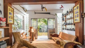 A room with wooden furniture, a large window, and a view of greenery outside. - Casa piscina e lazer 50m praia Lagoinha (Ubatuba)