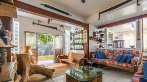 A spacious living area with a wooden coffee table, a colorful sofa, and a large window with a view of greenery. - Casa piscina e lazer 50m praia Lagoinha (Ubatuba)