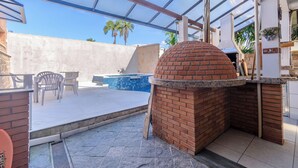 A brick oven with a glass enclosure, a pool, and outdoor seating. - Casa piscina e lazer 50m praia Lagoinha (Ubatuba)