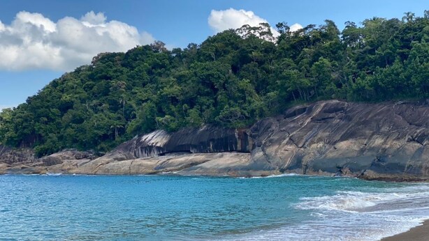 A beach with clear turquoise water, a sandy shore, and a forested cliff in the background. - Casa piscina e lazer 50m praia Lagoinha (Ubatuba)