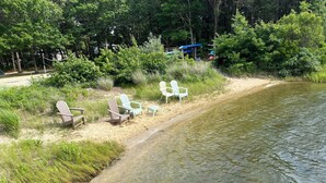 A lakeside area with several Adirondack chairs and a small dock. - Cute, cozy and newly built bungalow on private street awaits your Capecod visit. (Mashpee)